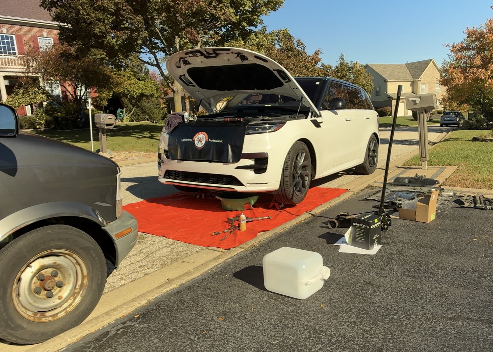 White Range Rover raised for mobile service with tools and a protective ground covering